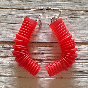 May include: A pair of red accordion-style earrings with silver hooks. The earrings are made of a flexible material and have a unique, modern design.