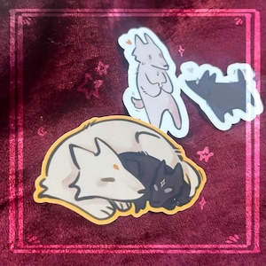 May include: A collection of stickers featuring cartoon wolves. One sticker shows a light tan wolf cuddling a black wolf. Two other stickers show a light pink and a black wolf. The stickers are on a burgundy background with a pink border.