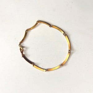 May include: A gold-toned bracelet composed of several curved, rectangular metal links connected by small circular rings. The bracelet features a secure lobster claw clasp mechanism, creating a continuous circular shape with a polished finish.
