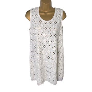 May include: White sleeveless dress with a floral eyelet pattern. The dress has a scoop neckline and a relaxed fit. The eyelet design is consistent throughout the dress, creating a delicate and airy look. The dress is displayed on a mannequin.
