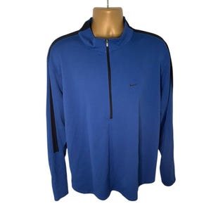 May include: A blue long-sleeve athletic shirt with a black zipper and black stripes down the sleeves. The Nike logo is visible on the chest. The shirt is displayed on a mannequin.