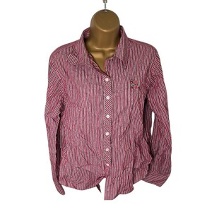 May include: A button-down shirt with vertical stripes in red, white, and black. The long-sleeved shirt has a collared neckline and a small embroidered design on the chest. The shirt is displayed on a mannequin.