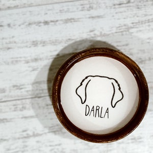 May include: A brown wooden frame with a white background and a black line drawing of a dog's head with the name "Darla" written underneath.