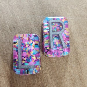 May include: Two resin letter tiles with a colourful confetti design. The letters are "L" and "R" in a white font.