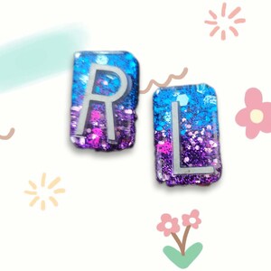 May include: Two resin letter tiles with a blue and purple glitter background. The letters are "R" and "L" in white.