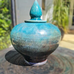 May include: A teal ceramic jar with a pointed lid. The jar has a mottled glaze with shades of blue, green, and brown.