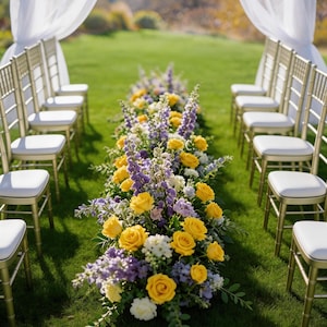Op de afbeelding: Een opstelling voor een trouwceremonie in de open lucht met rijen gouden stoelen met witte kussens. Een bloemstuk van gele rozen, paarse ridderspoor en witte bloemen omzoomt het gangpad op een groen gazon, met witte draperie&euml;n op de achtergrond.