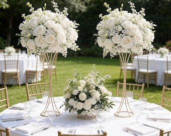 May include: Elegant outdoor wedding reception setup with round tables covered in white tablecloths. Each table is adorned with gold chairs, glassware, silverware, and floral centerpieces featuring white roses and greenery.