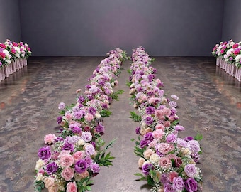 Könnte beinhalten: Zwei parallele Reihen von Blumen, hauptsächlich Rosen, in Lila-, Rosa- und Weißtönen, bilden einen Blumenweg. Die Blumen sind auf einem Betonboden angeordnet, mit zusätzlichen Blumenarrangements an den Seiten.