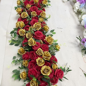 Könnte beinhalten: Ein Blumengesteck mit roten und goldenen Rosen und grünen Blättern. Die Rosen sind dicht gepackt, wodurch eine volle und lebendige Darstellung entsteht. Geeignet für Hochzeiten oder besondere Anlässe.