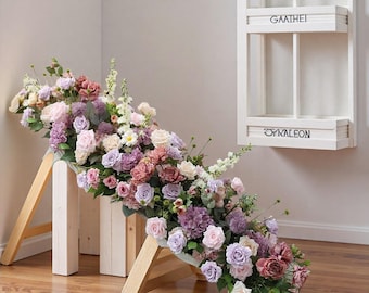 Könnte beinhalten: Blumenarrangement mit rosa, lila und weißen Blüten auf einem Holzgestell. Im Hintergrund ein weißes Wandregal mit den Schriftzügen "GAATHEI" und "OYKALEON".