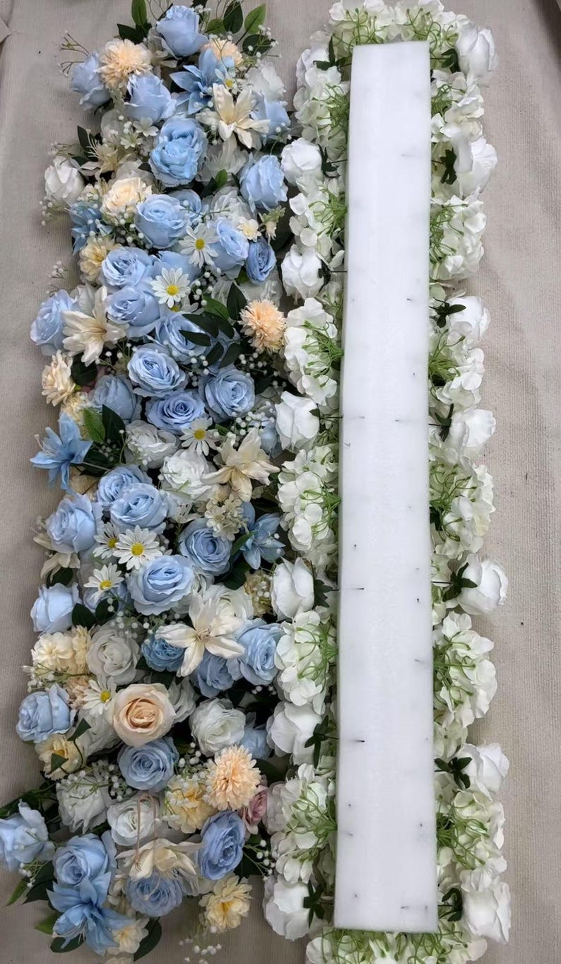 以下が含まれることがあります： ライトブルー、ホワイト、ペールピーチの造花のバラとデイジーを組み合わせたフラワーアレンジメント。中央を縦に長い長方形の白いフォームベースが貫いており、ピンで花の茎が固定されているのが見えます。