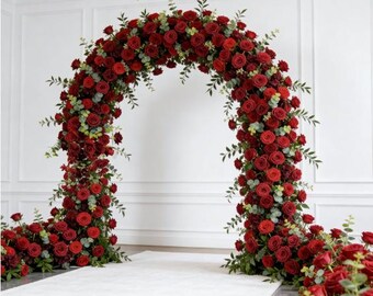 May include: A large, arch-shaped floral arrangement composed of vibrant red roses and green foliage. The arch is set against a white backdrop, creating a striking visual for weddings or special events. The arrangement is lush and full, with a carpet of roses at the base.
