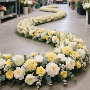 May include: A winding floral arrangement on a gray floor, featuring a mix of white and yellow flowers. The arrangement includes roses, hydrangeas, and other blooms, creating a visually appealing display. Green foliage accents the flowers, adding depth and texture to the design.