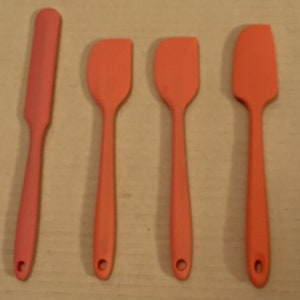 Könnte beinhalten: Vier orangefarbene Silikonspatel in verschiedenen Größen. Die Spatel haben eine abgerundete Kante und einen langen Griff.