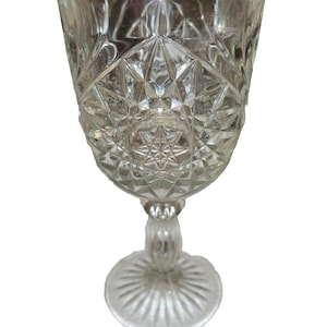 May include: A clear glass goblet with a cut glass design. The goblet has a round base and a tall stem.