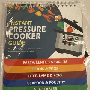 Op de afbeelding: Een spiraalgebonden Instant Pressure Cooker Guide met een donkerblauwe kaft en kleurrijke tabbladen. De kaft bevat illustraties van voedsel en een snelkookpan met een digitaal display met 07:12. Tabbladen vermelden categorieën zoals pasta, bonen en zeevruchten.