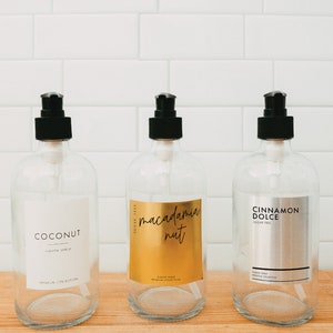 Puede incluir: Tres botellas de vidrio transparente con tapas de bomba negras y etiquetas. Las etiquetas son doradas, plateadas y blancas con el texto "Coconut", "Macadamia Nut" y "Cinnamon Dolce".