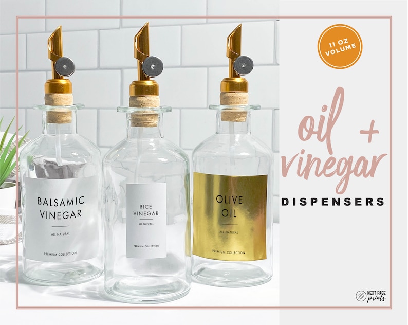 Puede incluir: Dispensadores de aceite y vinagre de vidrio transparente con boquillas doradas y tapones de corcho. Cada botella tiene una etiqueta: Vinagre Bals&aacute;mico, Vinagre de Arroz y Aceite de Oliva. La imagen tambi&eacute;n incluye el texto "oil + vinegar dispensers" y "11 OZ VOLUME".