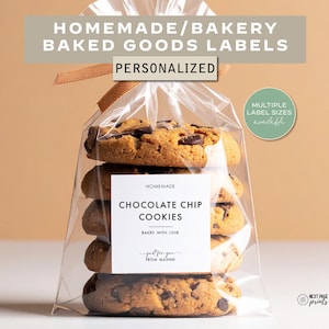 May include: A clear cellophane bag tied with a ribbon contains chocolate chip cookies. The label reads "Homemade Chocolate Chip Cookies, Baked with Love." Text at the top says "Homemade/Bakery Baked Goods Labels, Personalized." A green circle says "Multiple Label Sizes Available."