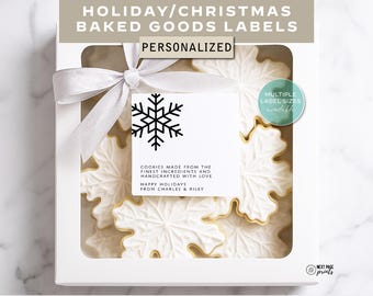 May include: A white box with a clear window, tied with a white ribbon, containing snowflake-shaped cookies. A tag with a black snowflake design and text that reads "Cookies made from the finest ingredients and handcrafted with love" is attached.