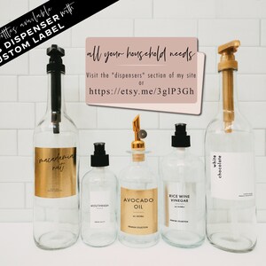 May include: Five glass bottles with pumps and labels. The labels are white with black text and include the names "macadamia nut", "mouthwash", "avocado oil", "rice wine vinegar", and "white chocolate". The bottles are on a white tiled background. The text "all your household needs" is on a pink rectangle in the upper right corner. The text "more bottles available GLASS DISPENSER with CUSTOM LABEL" is in the upper left corner.