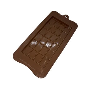 May include: A brown silicone chocolate mold with a rectangular shape and a grid pattern for creating individual chocolate squares. The mold has a small hole at the top for hanging.
