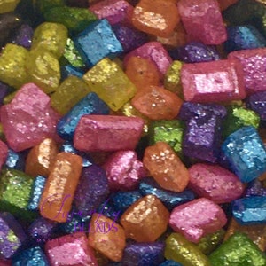 May include: A close-up shot of a collection of colourful, glittery, rectangular objects. The objects are in shades of pink, blue, green, yellow, orange, and purple. The text "Luxurious Blends" is visible. The objects are scattered.