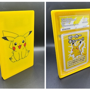 May include: Two yellow cases. One features a Pikachu illustration. The other case contains a Pokemon card with Japanese text and a Pikachu image. The card is graded as a 10.