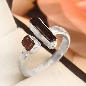 May include: A silver ring featuring two dark brown rectangular gemstones. One gemstone is set horizontally, and the other is set at an angle. The ring is displayed in a black jewelry box with a white interior.