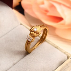 May include: Gold ring with two bands, featuring a design of two hands clasped together with a small diamond in the center. The ring is set with small diamonds around the hands.