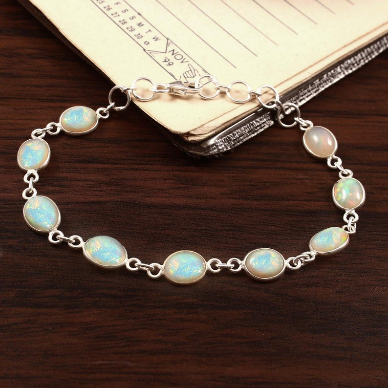 May include: A silver bracelet with a chain link design and oval-shaped opal stones. The bracelet has a lobster clasp closure.