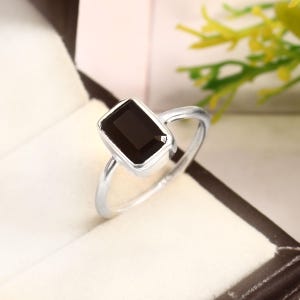 Puede incluir: Un anillo de plata con una piedra rectangular negra.