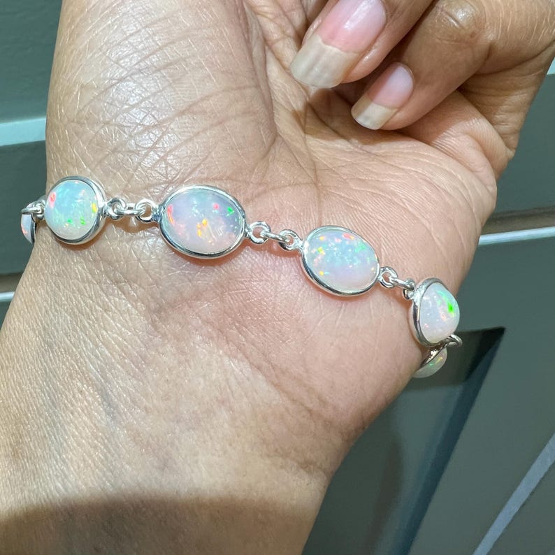 May include: A silver bracelet with five oval-shaped white opal stones. The bracelet is on a person's wrist.