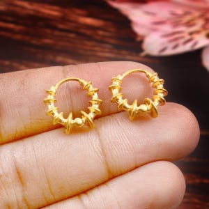 May include: A pair of gold hoop earrings with a textured, twisted design. The earrings are small and delicate.