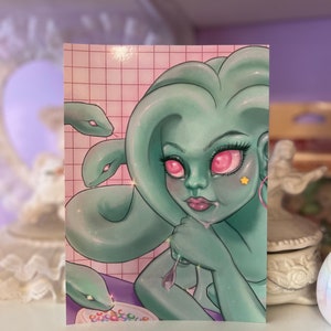 May include: Illustration of a Medusa-like figure with teal skin, pink eyes, and snake hair. She is holding a spoon over a bowl of cereal. The background is a pink grid pattern.