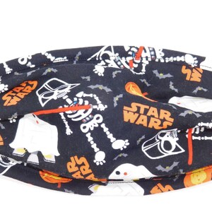 May include: Black fabric face mask with a Halloween and Star Wars theme. The mask features a skeleton, Darth Vader, bats, and the words "Star Wars".
