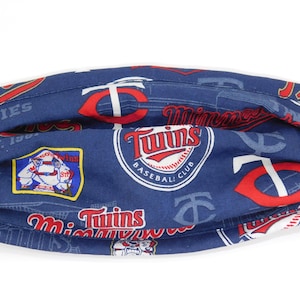 Könnte beinhalten: Eine blaue Stoffmaske mit einem sich wiederholenden Muster des Logos des Baseballteams Minnesota Twins. Das Logo zeigt die Worte "Twins Baseball Club" und einen Baseball. Die Maske zeigt auch die Worte "Twin Cities Est. 1961" und "Minnesota Twins".