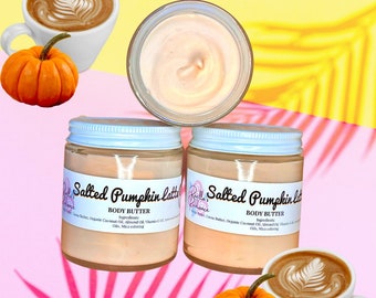 May include: Two jars of salted pumpkin latte body butter with a white lid and a label that says "Salted Pumpkin Latte Body Butter" and lists the ingredients. The jars are on a pink and yellow background with a pumpkin and a cup of coffee.
