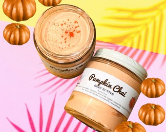 May include: Two glass jars of Pumpkin Chai Body Butter with a label that reads "Pumpkin Chai Body Butter" and lists the ingredients. The jars are surrounded by small orange pumpkins.