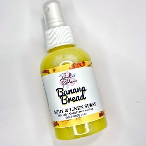 May include: A yellow bottle with a white spray nozzle and a white label that says "Borella's Radiance Banana Bread BODY & LINEN SPRAY Skin Safe | Alcohol Free | Sensitive Skin Friendly | 4 oz."
