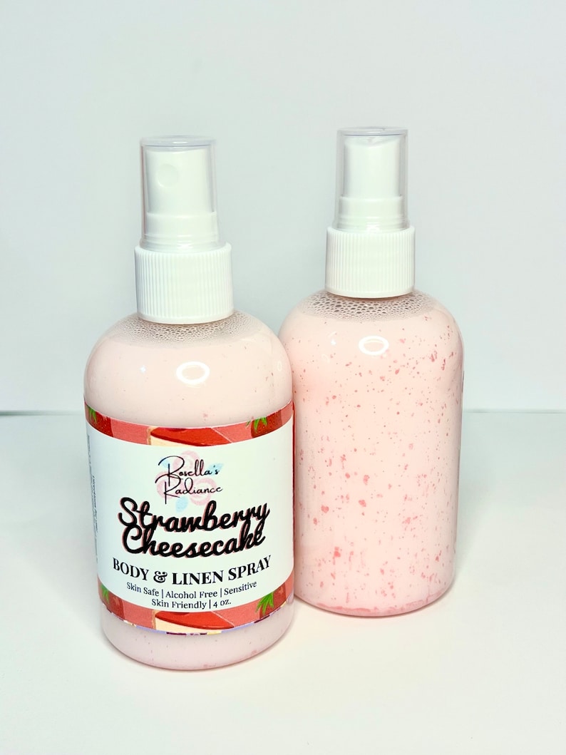 Puede incluir: Dos botellas transparentes con tapas de pulverizaci&oacute;n blancas llenas de un l&iacute;quido rosa. La etiqueta de la botella dice "Buella's Radiance Strawberry Cheesecake BODY & LINEN SPRAY Skin Safe | Alcohol Free | Sensitive Skin Friendly | 4 oz."