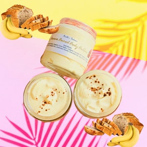 Op de afbeelding: Twee glazen potten met bananenbrood body butter op een gele en roze achtergrond. De potten zijn gevuld met een lichtgele crème en hebben een bruin deksel. De potten zijn omringd door bananenplakjes en bananen.