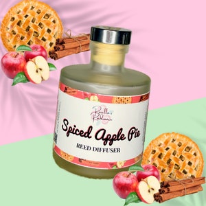 Può includere: Una bottiglia di vetro trasparente con un tappo argentato e un'etichetta che recita "Rosellla's Radiance Spiced Apple Pie Reed Diffuser". La bottiglia è circondata da mele, bastoncini di cannella e crosta di torta di mele.