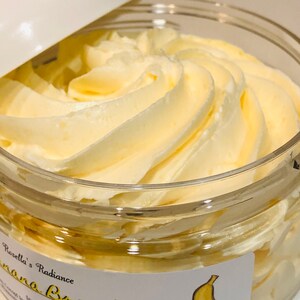 May include: A jar of Rosella's Radiance Banana Bread Whippin' Wash. The product has a whipped, creamy texture and a light yellow colour. The jar is clear with a white lid. A label with a banana illustration is visible.