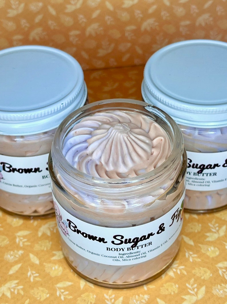 Puede incluir: Tres frascos de vidrio con tapas blancas llenos de manteca corporal marr&oacute;n claro y p&uacute;rpura. Los frascos est&aacute;n etiquetados como "Brown Sugar & Fig" y "Body Butter". Los ingredientes se enumeran como: Manteca de cacao, aceite de coco org&aacute;nico, aceite de almendras, aceite de vitamina E, colorante mica.