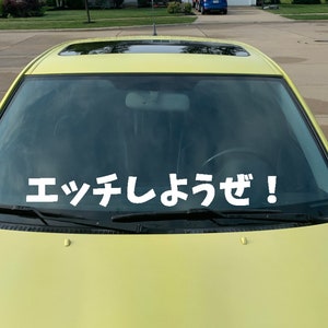 Puede incluir: Un coche amarillo con techo solar y una pegatina en el parabrisas. La pegatina blanca tiene caracteres japoneses. El coche está aparcado en una calle residencial.