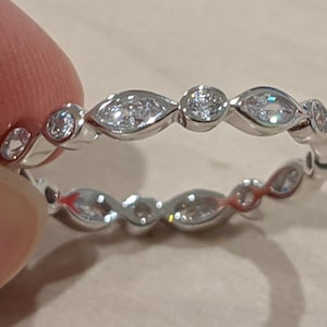 May include: A silver band ring with a row of small, clear, marquise-shaped stones and a larger round stone in the center.