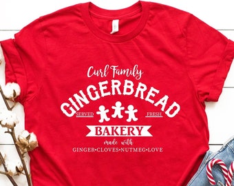 May include: Red t-shirt with a white graphic that says "Curl Family Gingerbread Bakery" with three gingerbread people and the text "Served Fresh Made with Ginger-Cloves-Nutmeg-Love".