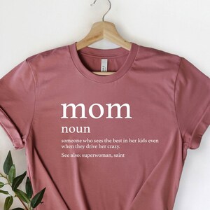 May include: A maroon t-shirt with the word "mom" in white text, defined as "someone who sees the best in her kids even when they drive her crazy. See also: superwoman, saint."